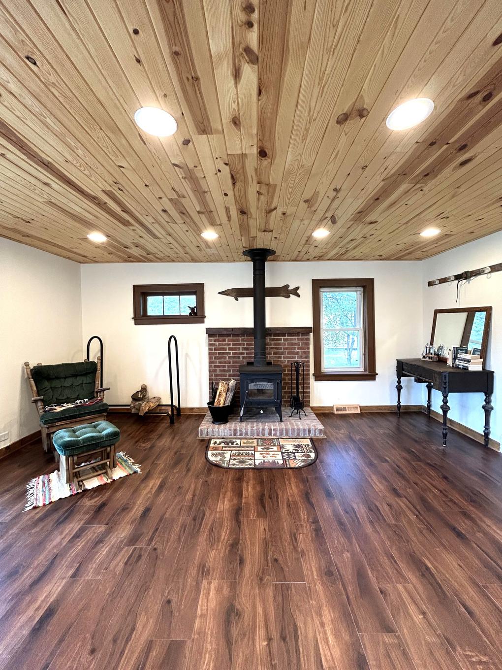 Living room with knotty pine ceiling, brick hearth, and wood stove