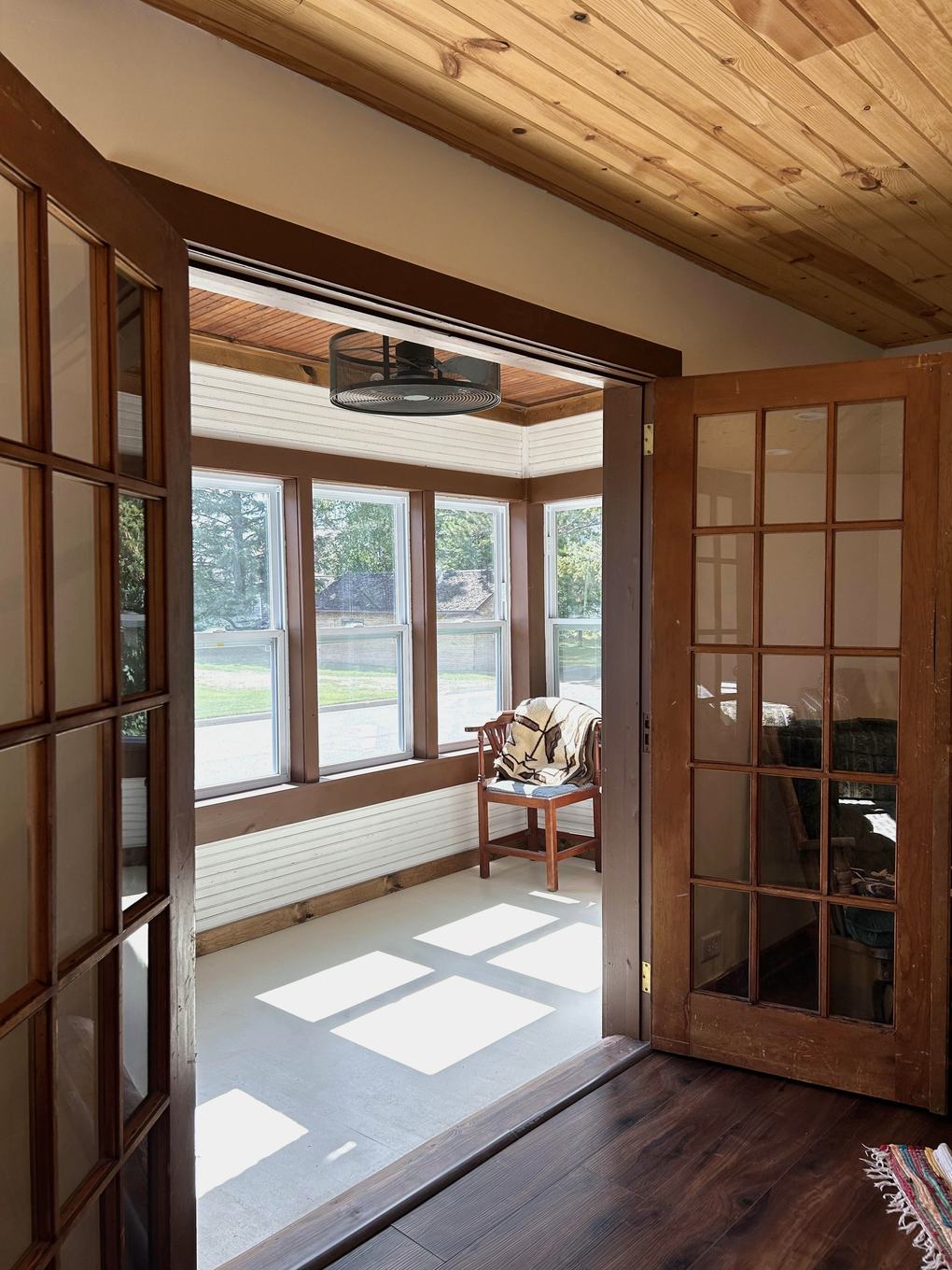 Three-season porch with French doors open and a wicker chair